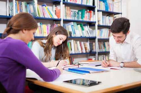 Drei Studierende in einer Bibliothek auf einem Tisch beim Lernen