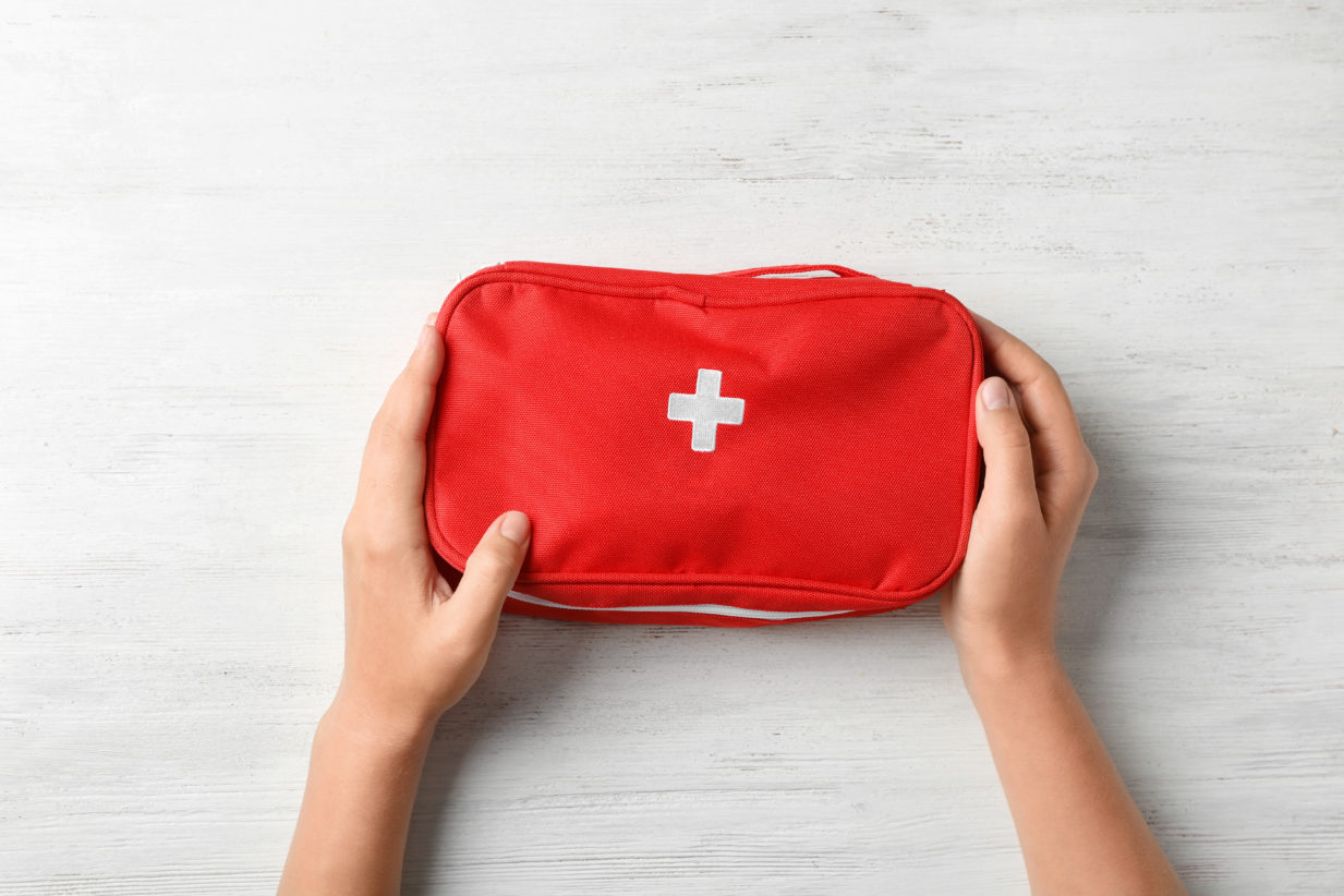 zwei Hände halten eine rote Erste-Hilfe-Tasche mit einem weißen Kreuz in der Mitte