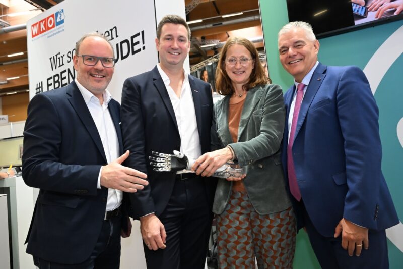 Gruppe mit Ausstellenden und Besuchenden posen für Foto mit Roboter-Hand