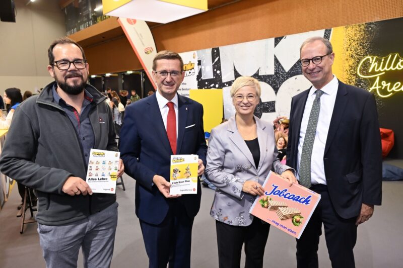 Vertreterinnen und Vertreter zeigen Messebroschüren