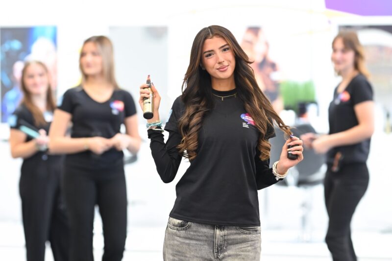 Mädchen posiert bei Messestand mit Frisörinnen
