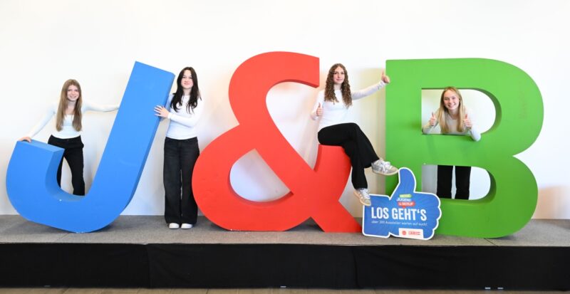 Mädchen posieren vor großen Messe-Buchstaben