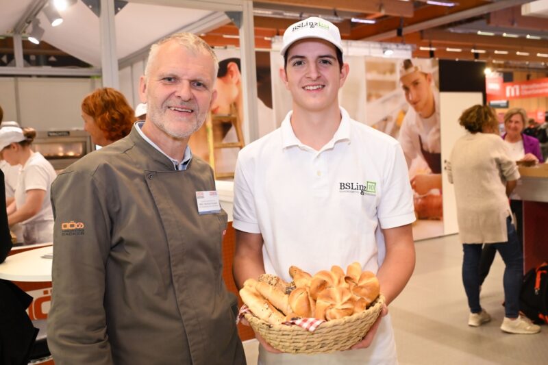 Lehrling zeigt Korb mit frischem Gebäck auf der Messe
