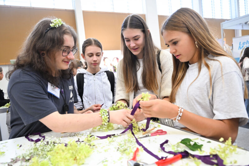 Jugendliche binden Armbänder aus Blumen bei Messestand