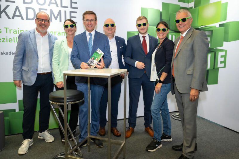 Vertreter der WKO und des Landes OÖ mit grünen Sonnenbrillen beim Messestand der Dualen Akademie