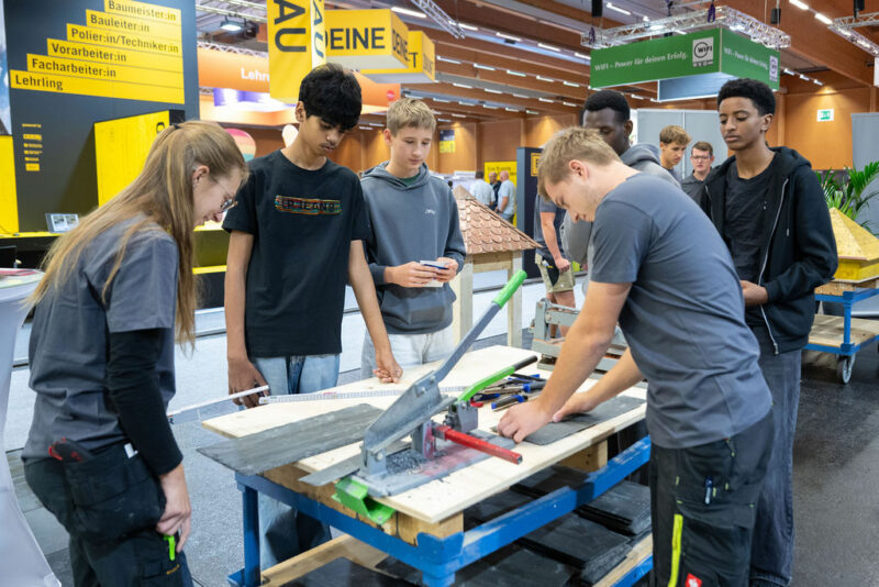 Jugendliche beobachten einen Aussteller, der ein Werkstück bearbeitet