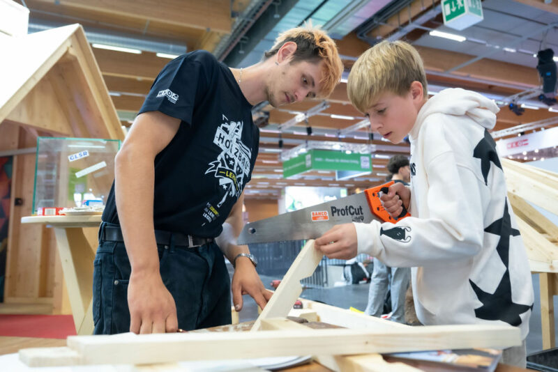 Junge sägt konzentriert Werkstück bei Messestand