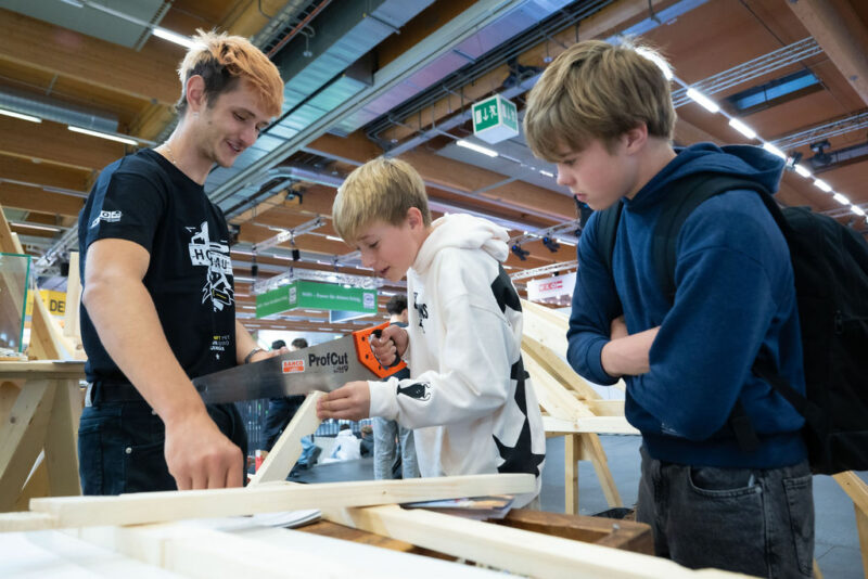 Junge sägt begeistert Werkstück bei Messestand