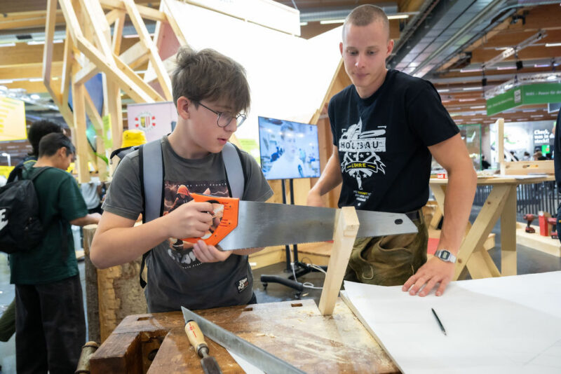 Junge sägt Werkstück bei Messestand